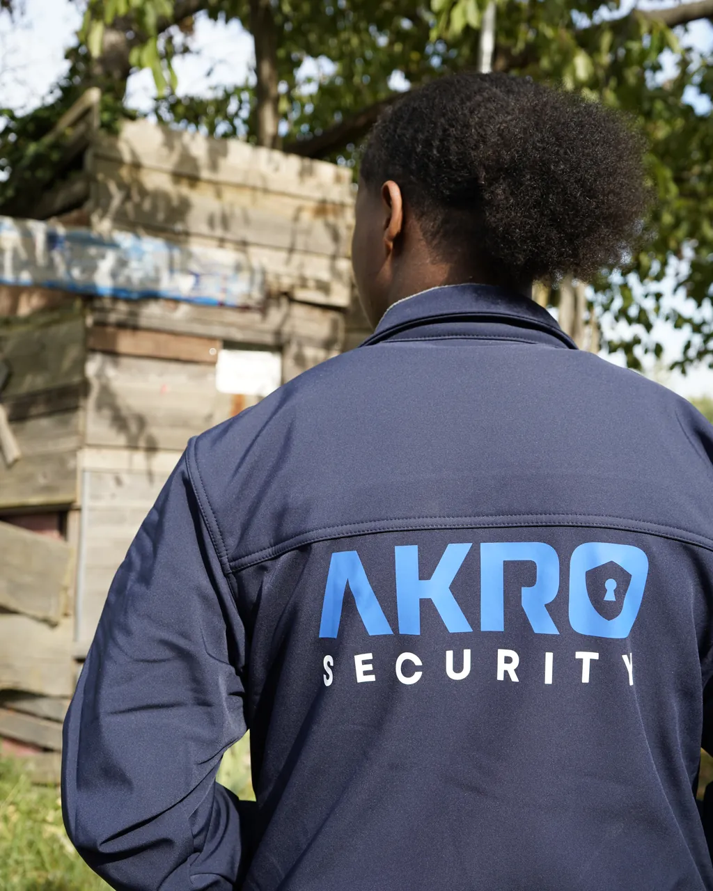 Mitarbeitende von AKRO Security in Jacke mit Logo, von hinten, vor einer Holzhütte
