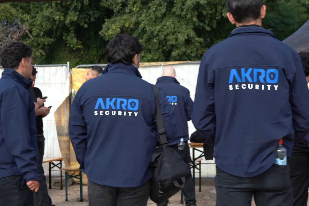 Mehrere Mitarbeitende von AKRO Security in Jacken mit Logo, von hinten, vor einem Einsatz